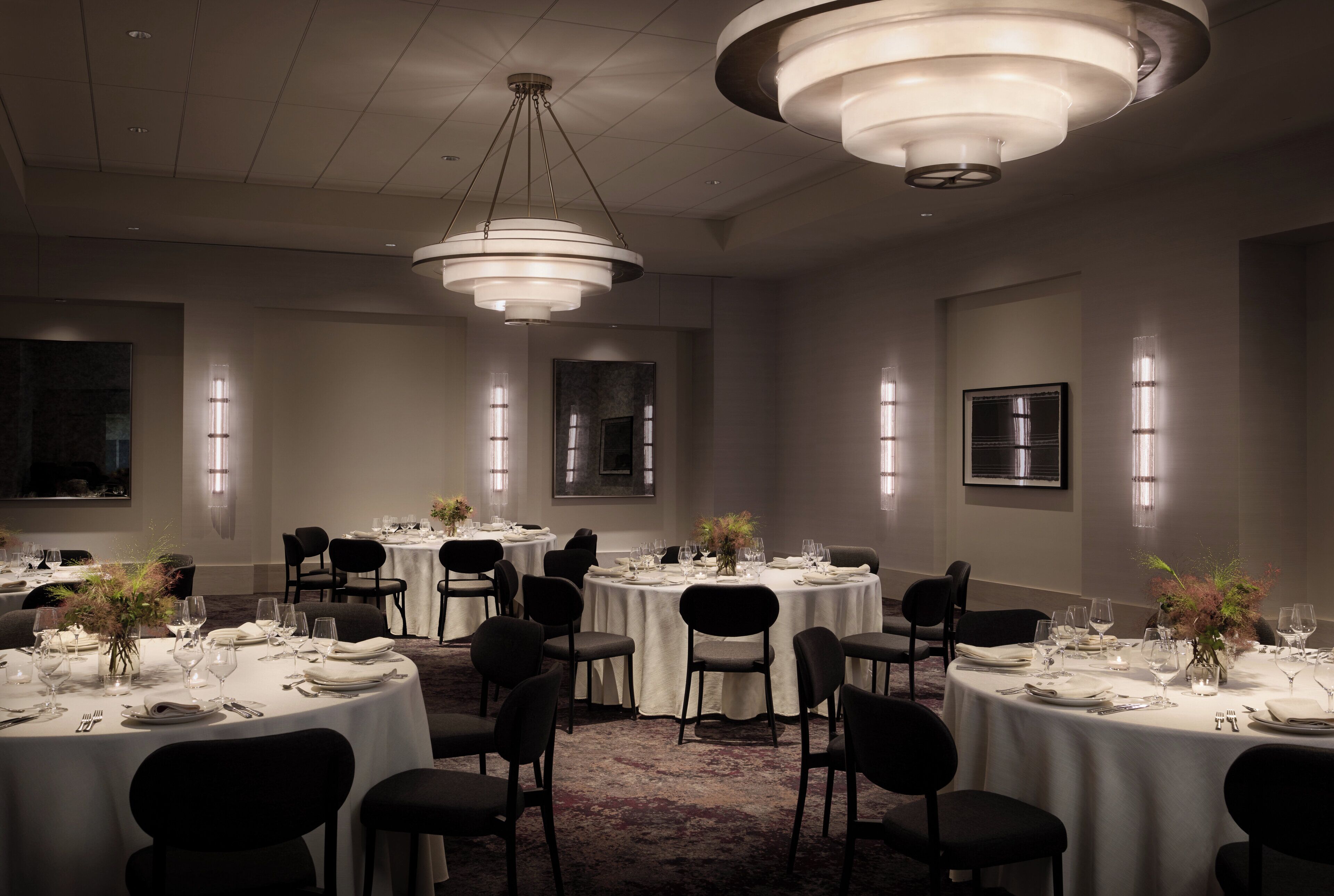 Un comedor formal con varias mesas redondas, sillas negras y candelabros modernos.