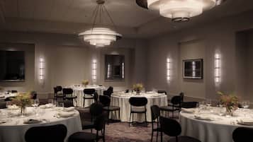 Un comedor formal con varias mesas redondas, sillas negras y candelabros modernos.