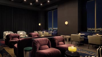 Un salón moderno con asientos cómodos, iluminación ambiental y vistas a la ciudad a través de amplias ventanas.