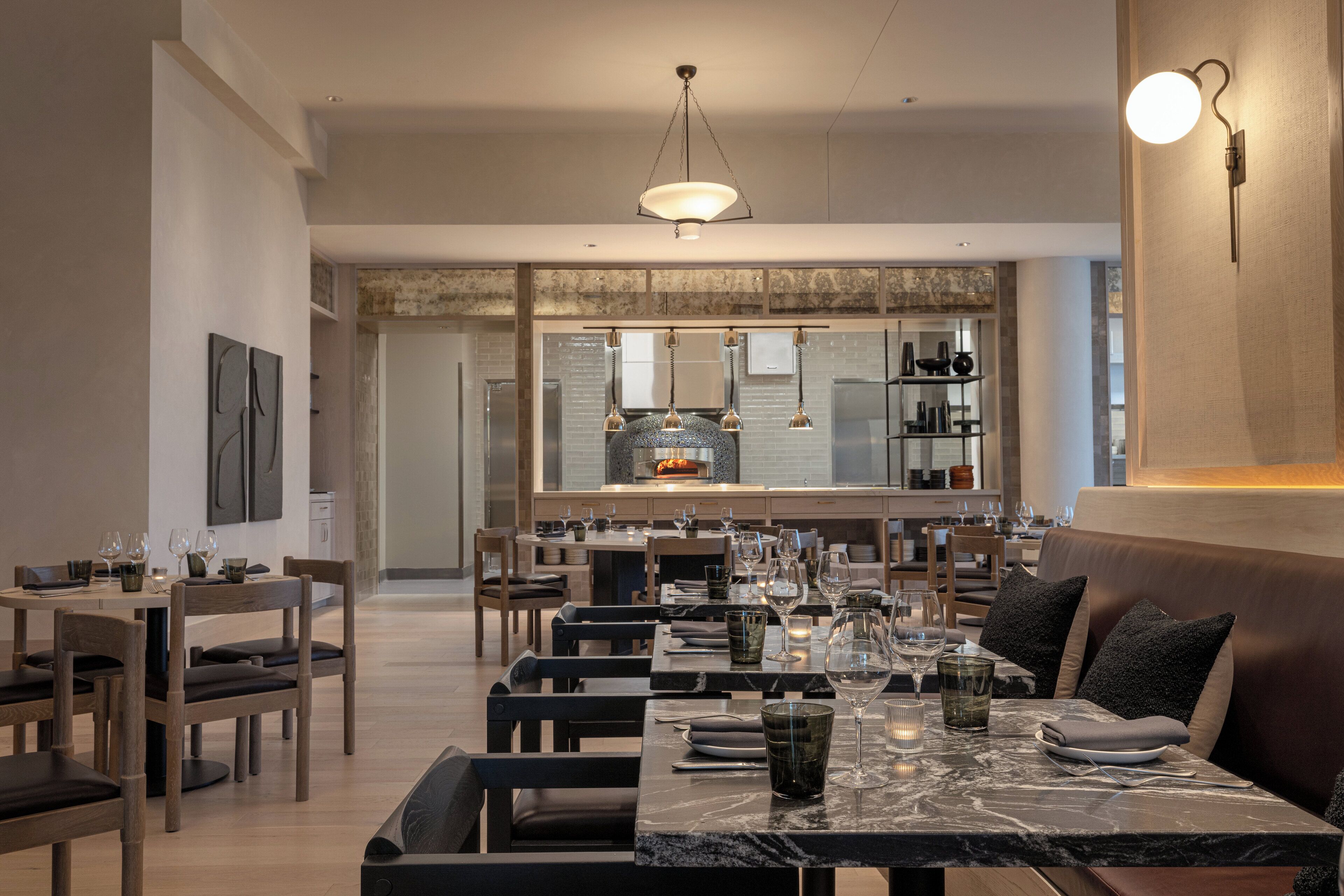 A modern dining area with marble tables, wooden chairs, and a central fireplace.