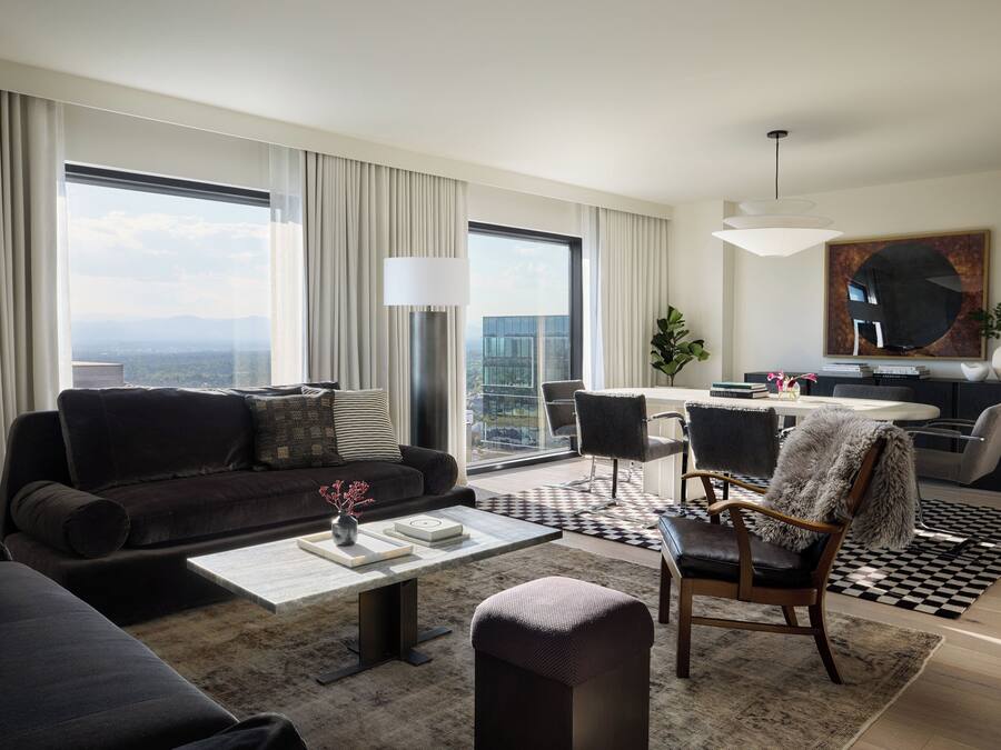 A modern living room with a sofa, coffee table, and chairs, a dining area with a table and chairs, and a large window with curtains.