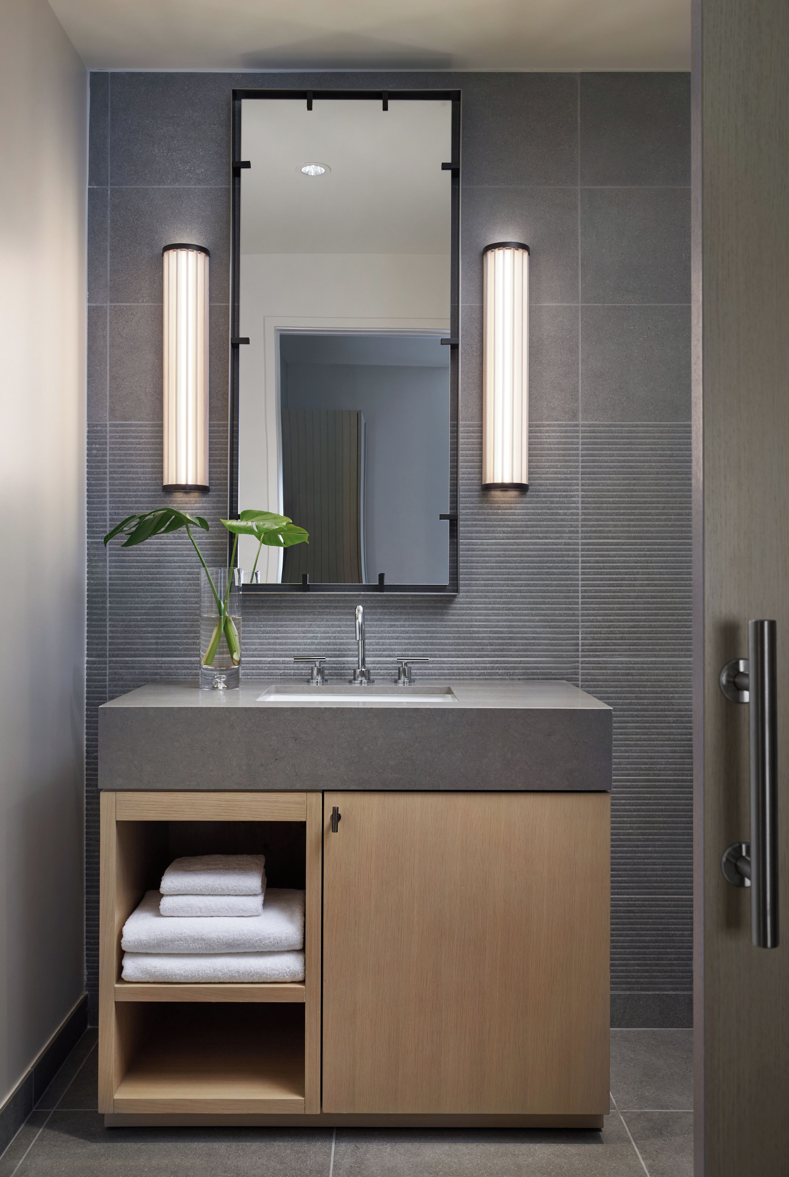 Un baño moderno con un tocador de madera, un espejo grande y dos luces empotradas.