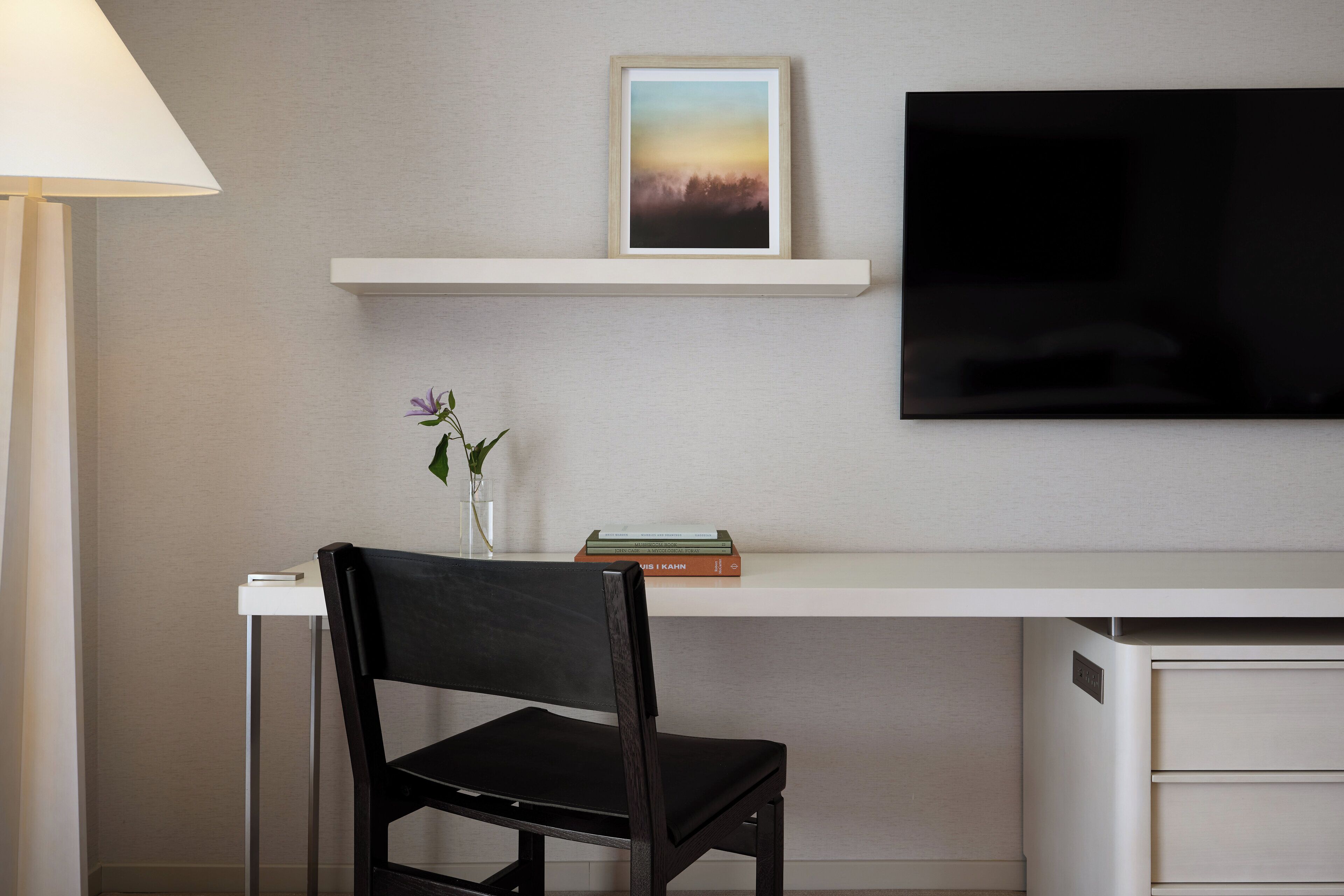 Een moderne kamer met een bureau, stoel, televisie en een plank met een ingelijst kunstwerk en boeken.