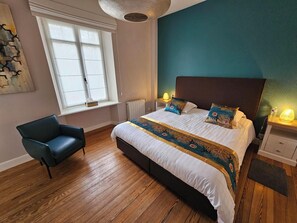A bedroom with a large bed, a chair, a window, and a wall with a textured design. - L'Albizia Maison d'Hôtes (Libin)