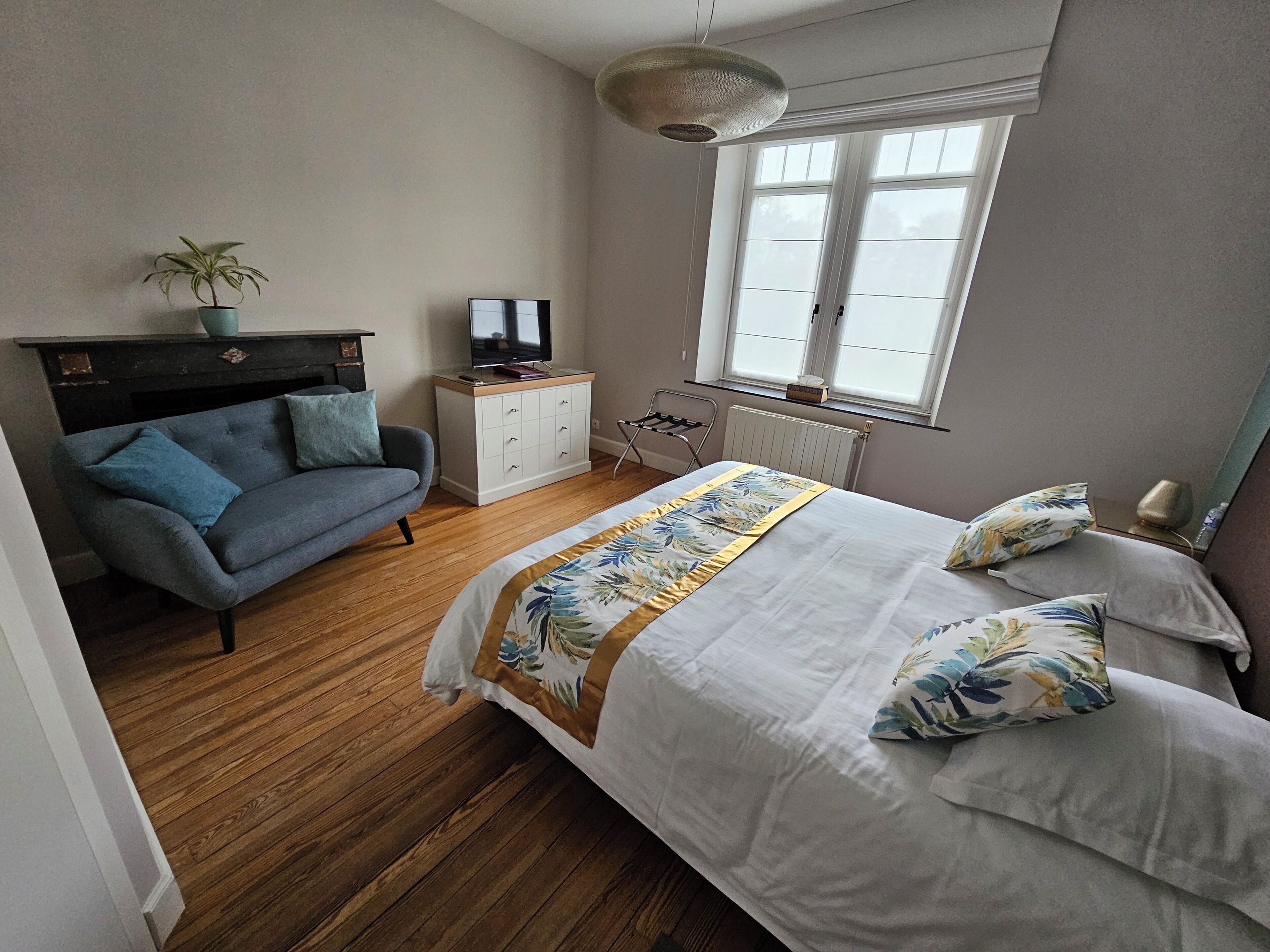 A bedroom with a bed, a sofa, a TV, a radiator, and a window.