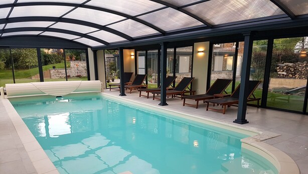 An indoor swimming pool with clear water, surrounded by lounge chairs and a glass ceiling. - L'Albizia Maison d'Hôtes (Libin)