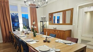 A dining room with a long wooden table set for six, flanked by chairs, with a chandelier above. - L'Albizia Maison d'Hôtes (Libin)