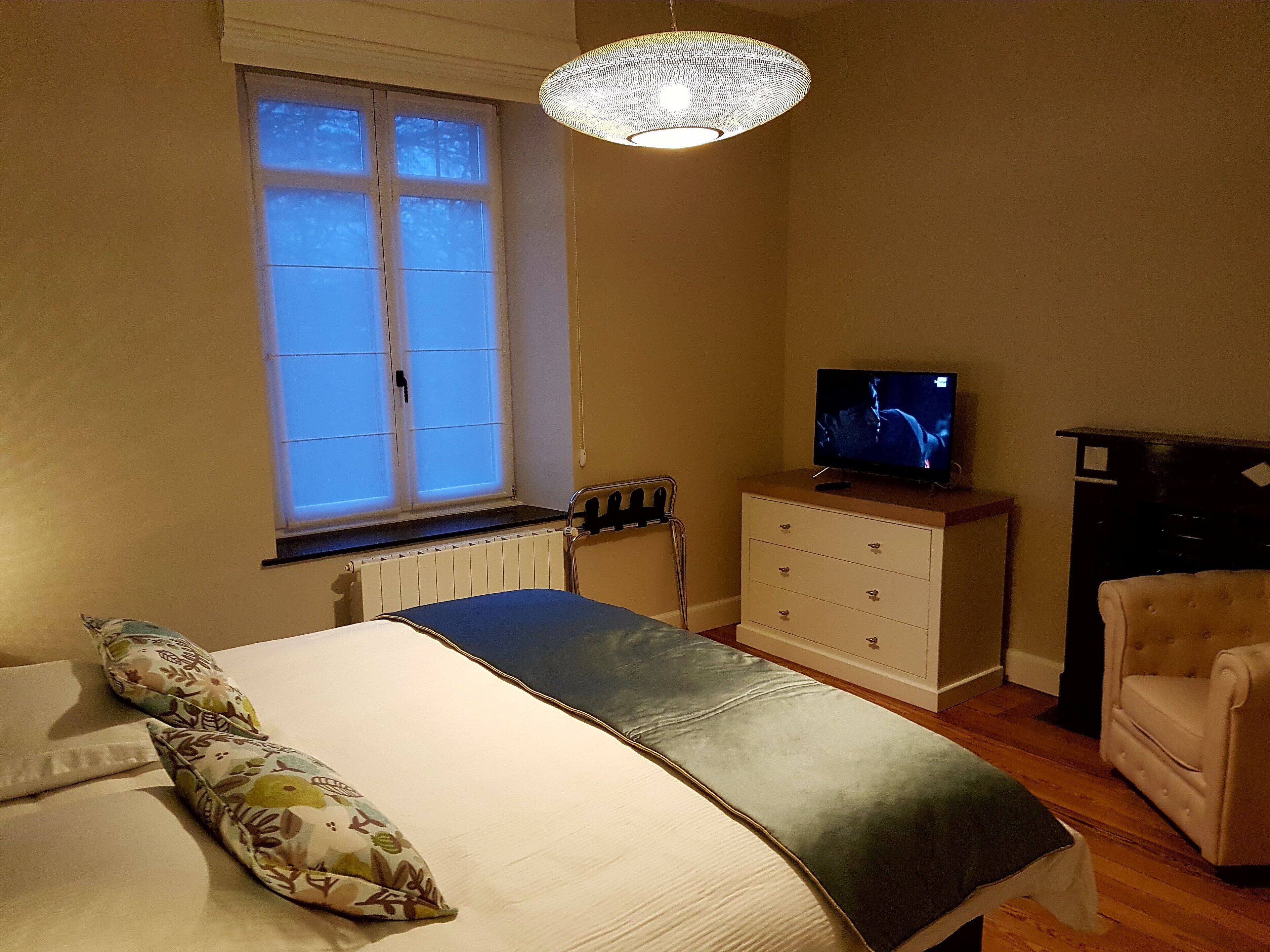 Une chambre à coucher avec un lit, une commode, un téléviseur, une chaise et une fenêtre.