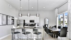 A modern kitchen with white cabinets, stainless steel appliances, and pendant lighting.