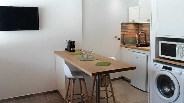 Eine kleine Küche mit einem Holztisch, zwei Barhocker, einer Waschmaschine und einer Mikrowelle.