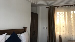 A hotel room with a bed, a wooden wardrobe, a ceiling fan, and a window with curtains.