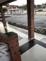 Un espacio exterior cubierto con suelo de baldosas, pilares de ladrillo y una pared de piedra.