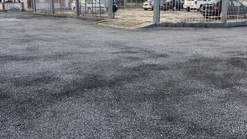 Un área de estacionamiento con superficie de grava, entrada protegida por una reja y un edificio de fachada de ladrillo.