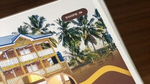 A hotel advertisement featuring a room with a bed, a window, and a view of palm trees. The text includes "Down Town Virgins Hotel," "Enjoy a Luxury Experience," and contact information.