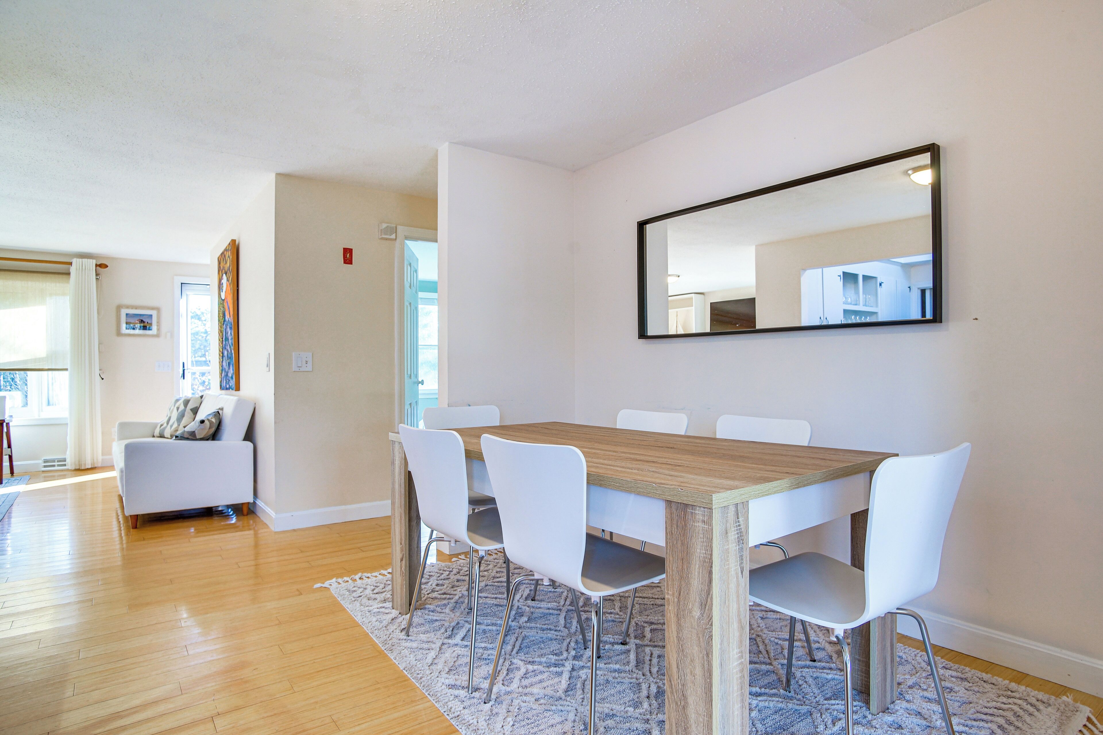A dining area with a wooden table, white chairs, and a large mirror on the wall.