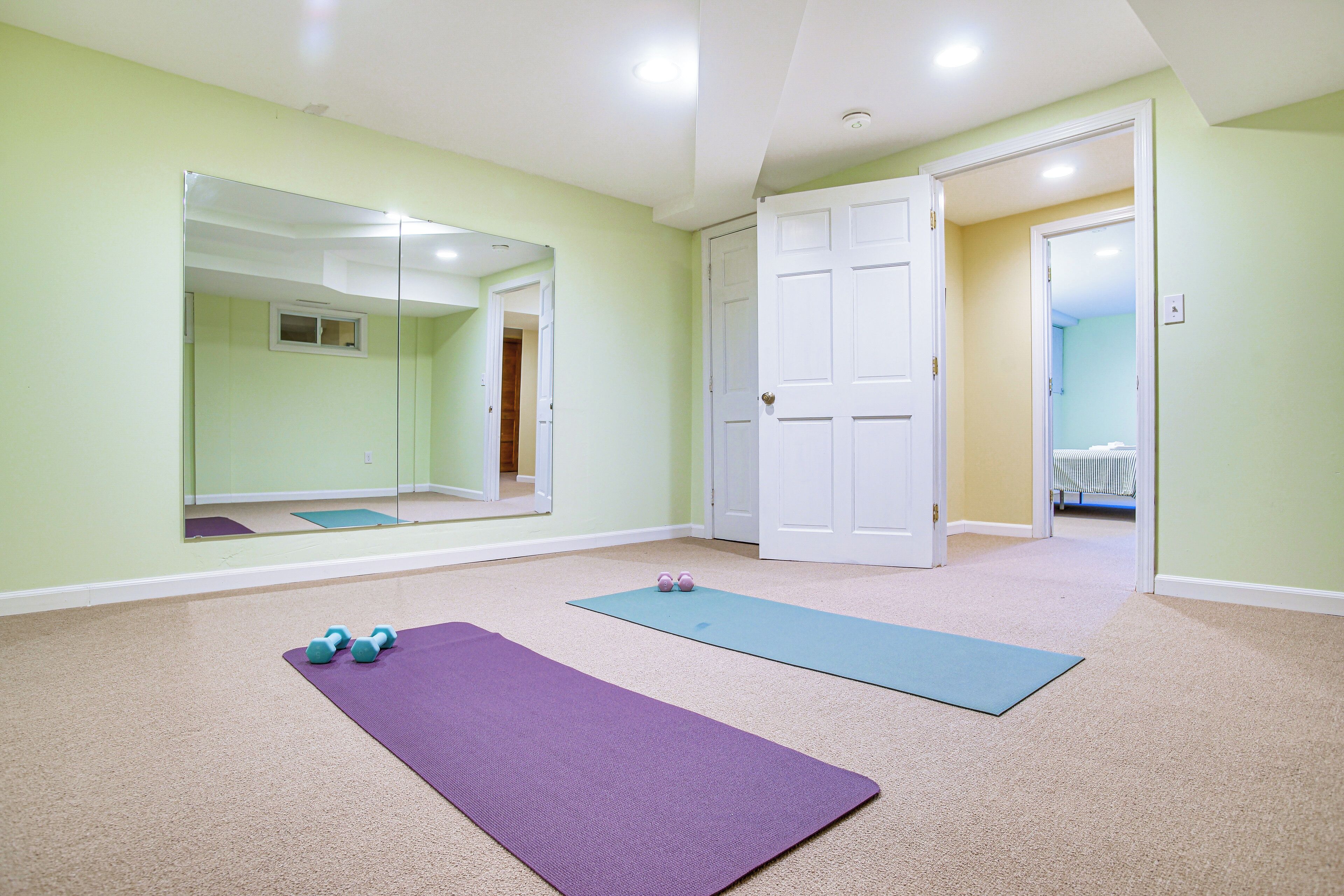 Une pièce avec un grand miroir, deux tapis de sol pour les exercices et une paire d’haltères.