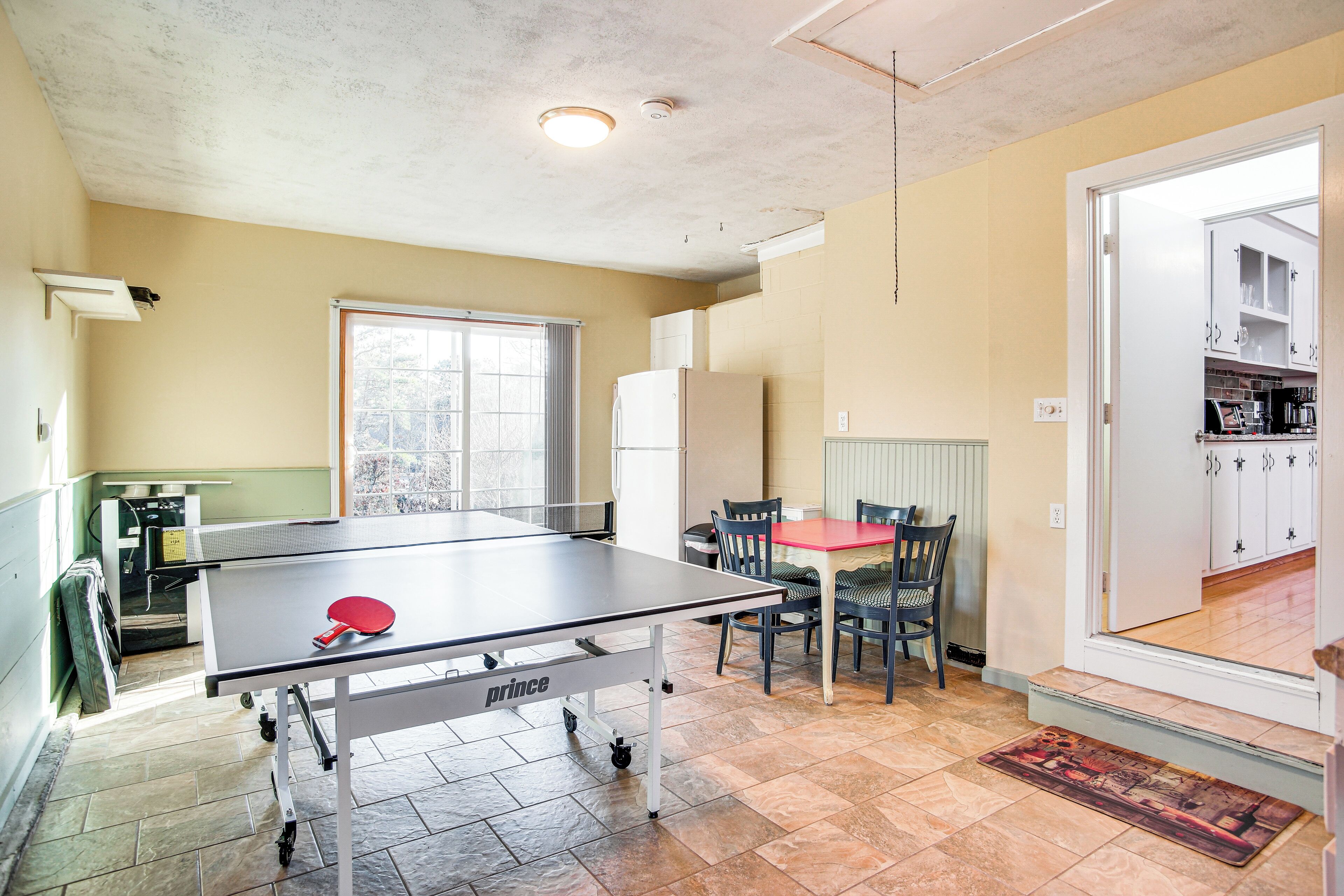 Una habitación con mesa de ping pong, sillas, una ventana y una zona de cocina.