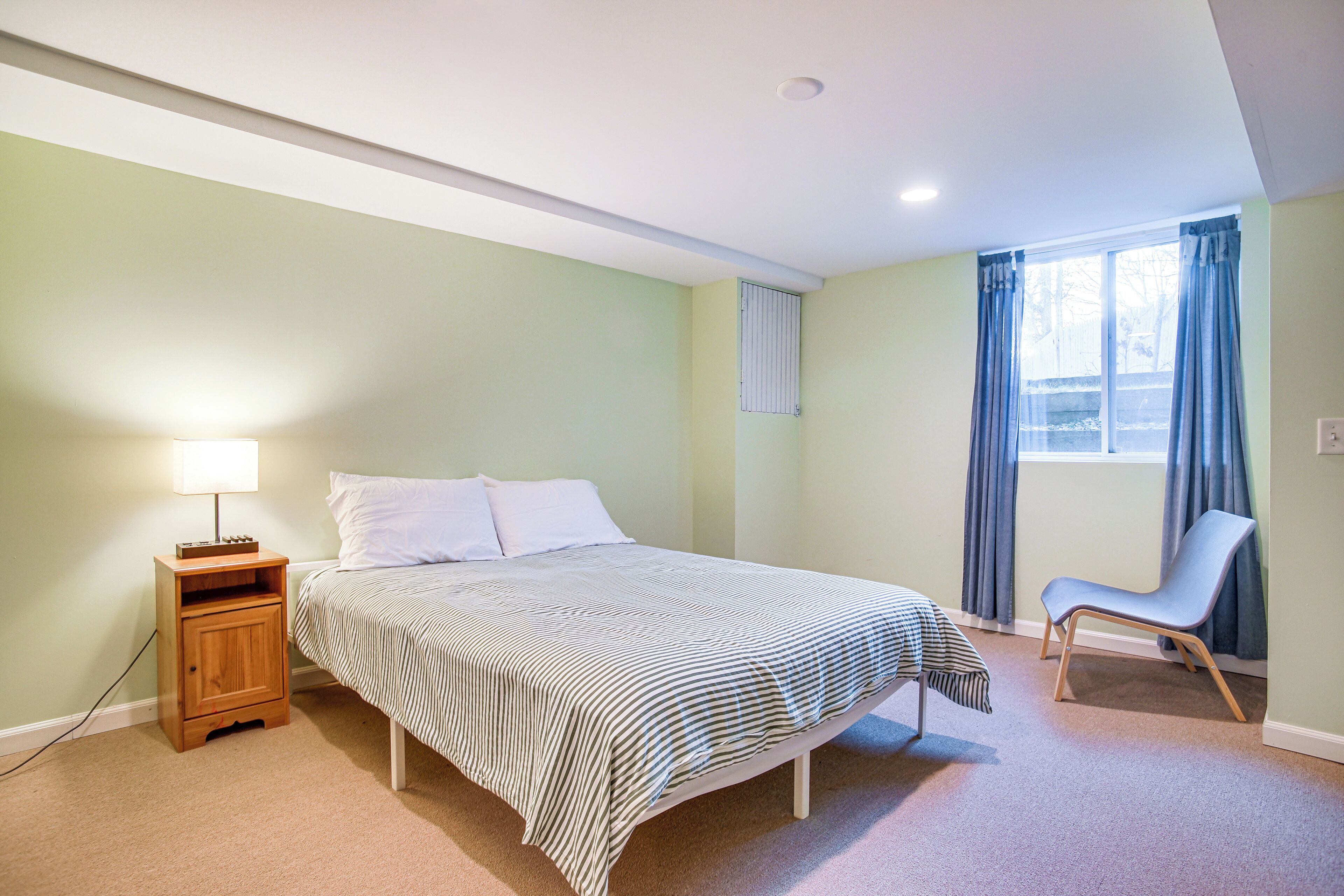 A bedroom with a bed, bedside table, chair, and a window with curtains.