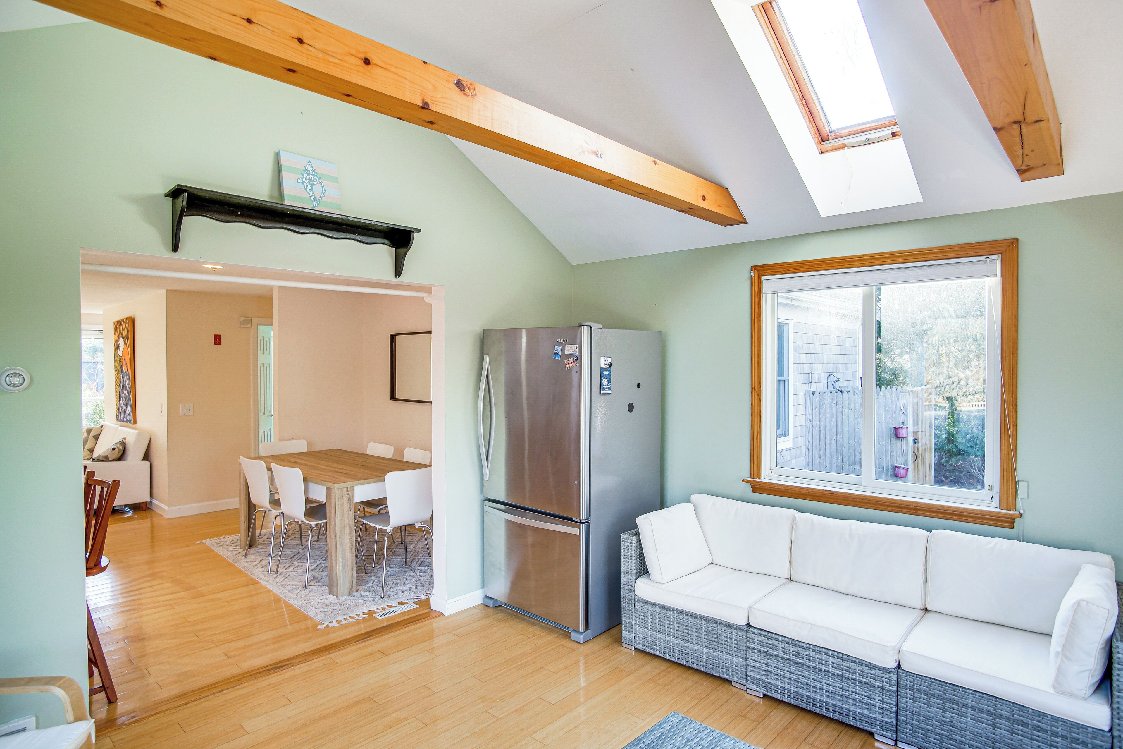 A modern kitchen with a built-in stainless steel refrigerator, a dining area with a wooden table and chairs, and a white sofa.