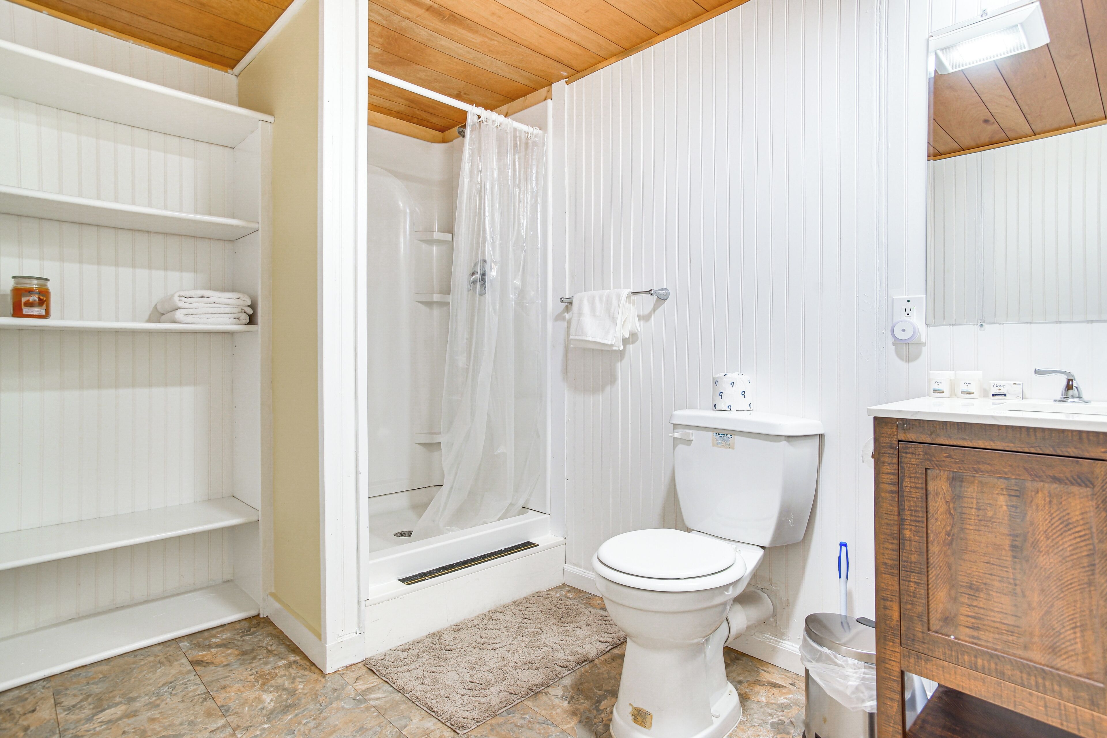 A bathroom with a shower, toilet, and wooden vanity.