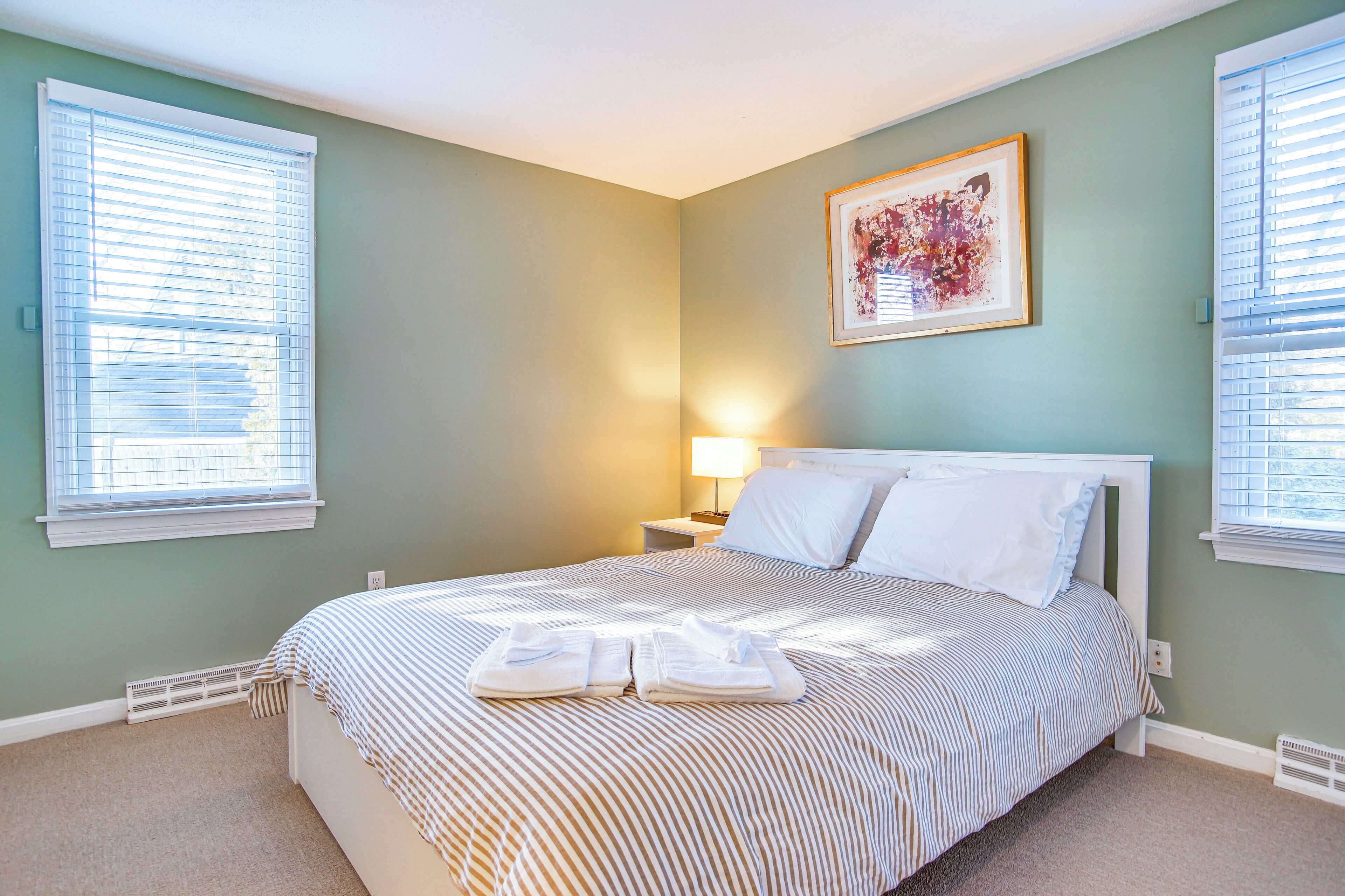 A neatly made bed with striped bedding, a bedside lamp, and a framed artwork on the wall.