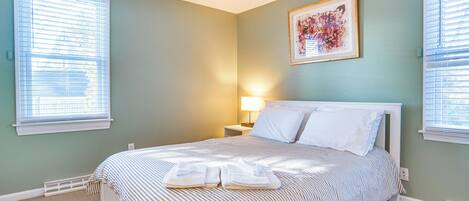 A neatly made bed with striped bedding, a bedside lamp, and a framed artwork on the wall.