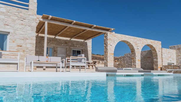 A pool area with stone walls and a pergola, outdoor seating, and a clear blue sky. - Aegean Feelings (Paros)