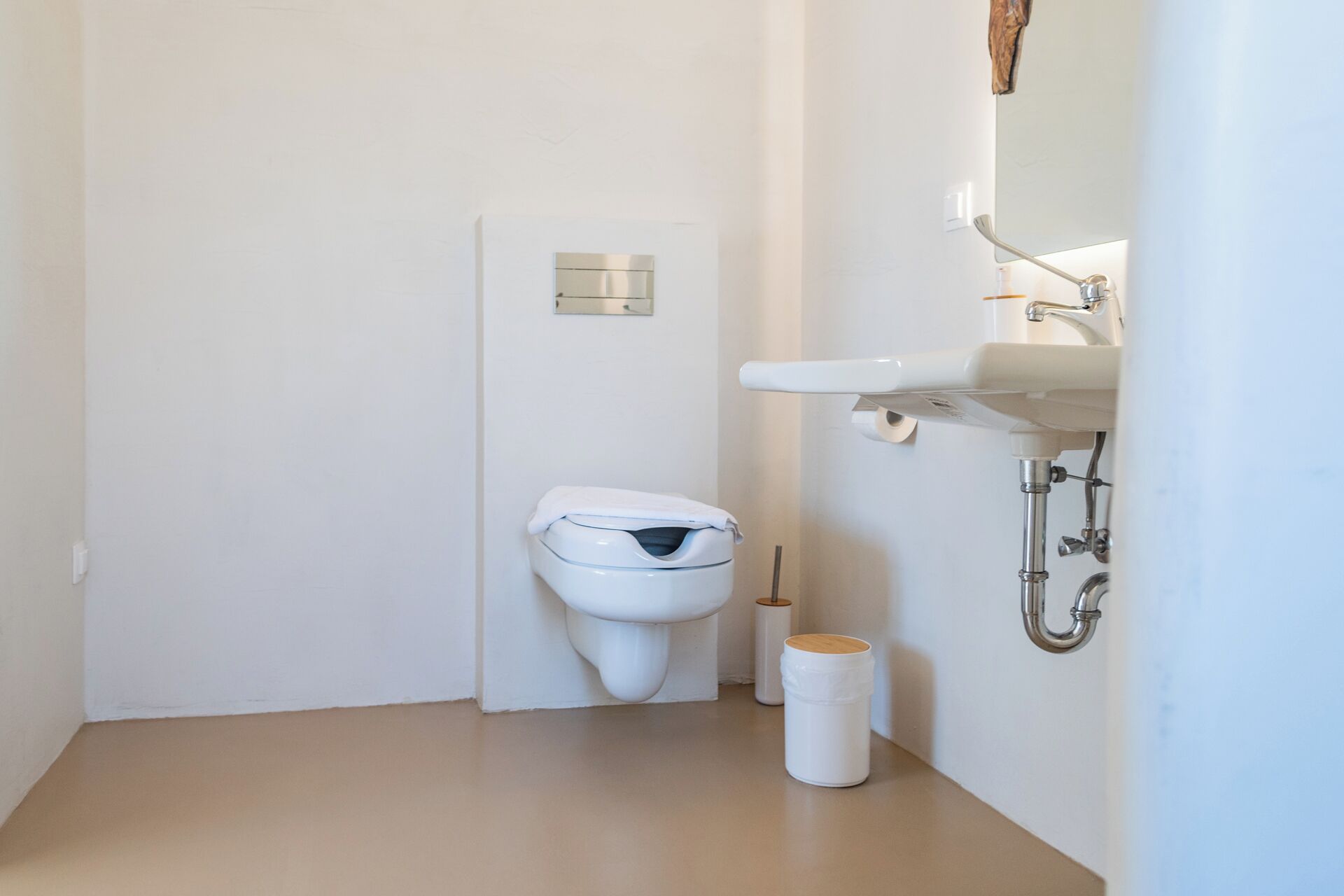 A small, modern bathroom with a white toilet, a white sink, and a toilet paper holder.