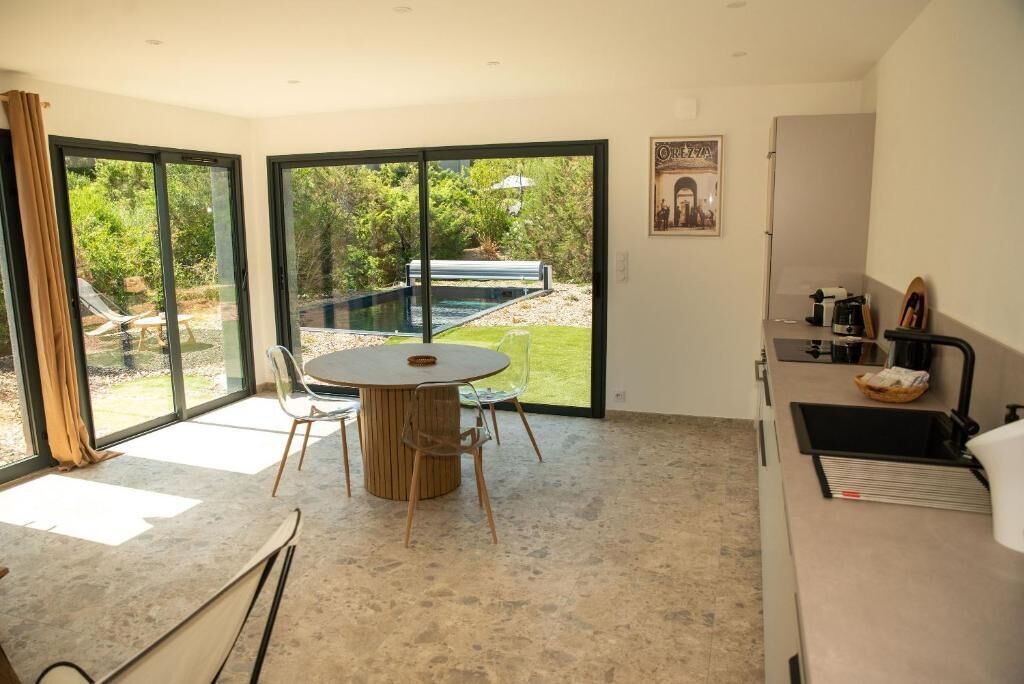 A modern kitchen with a dining area, large sliding glass doors, and a view of a swimming pool.
