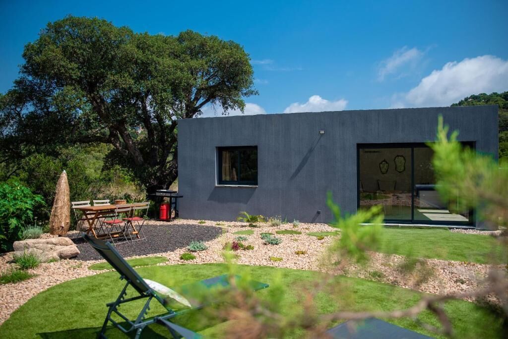 Et moderne hus med mørk facade, en velplejet have og en terrasse med udendørs møbler.
