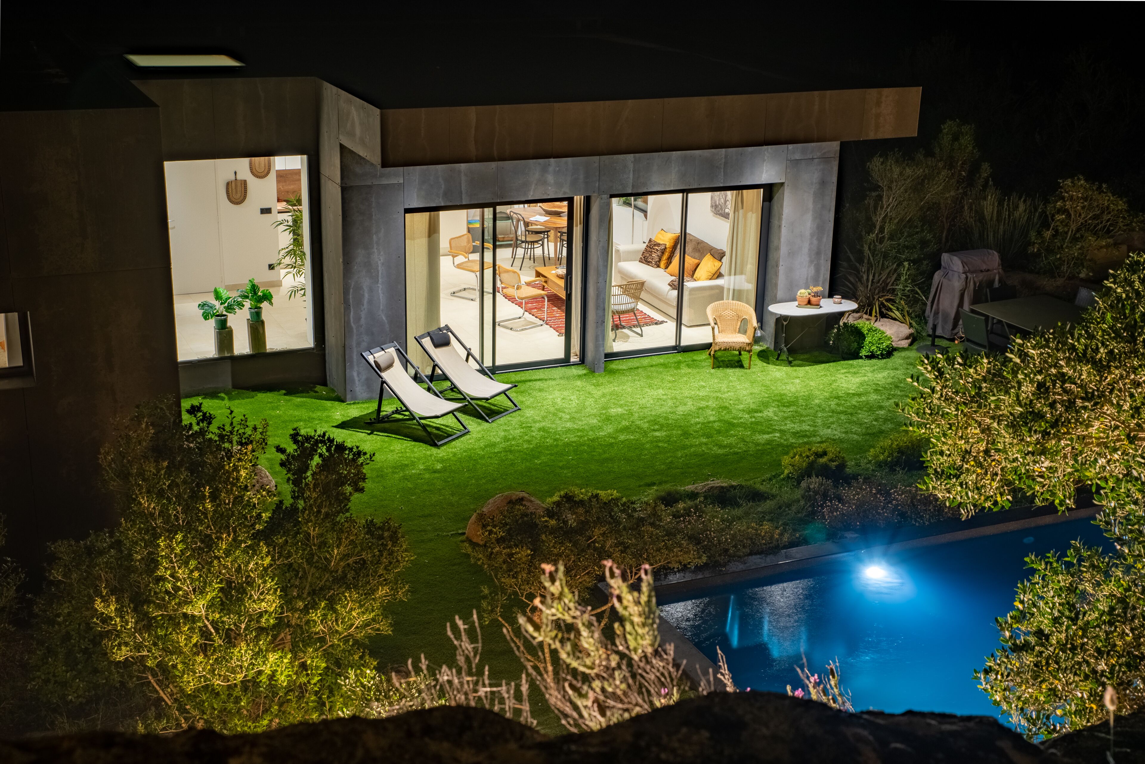 A modern house with a swimming pool, a patio with lounge chairs, and a well-maintained lawn.