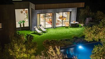 A modern house with a swimming pool, a patio with lounge chairs, and a well-maintained lawn.