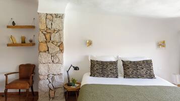 A bedroom with a stone wall, a bed with two pillows, a chair, and two wall-mounted shelves.