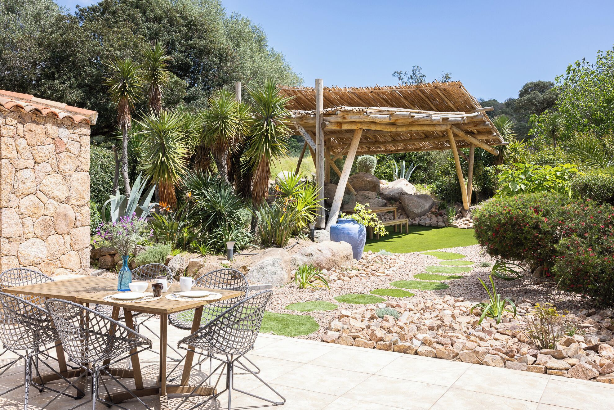 Een terras met een stenen muur, een houten pergola en een tafel met stoelen.