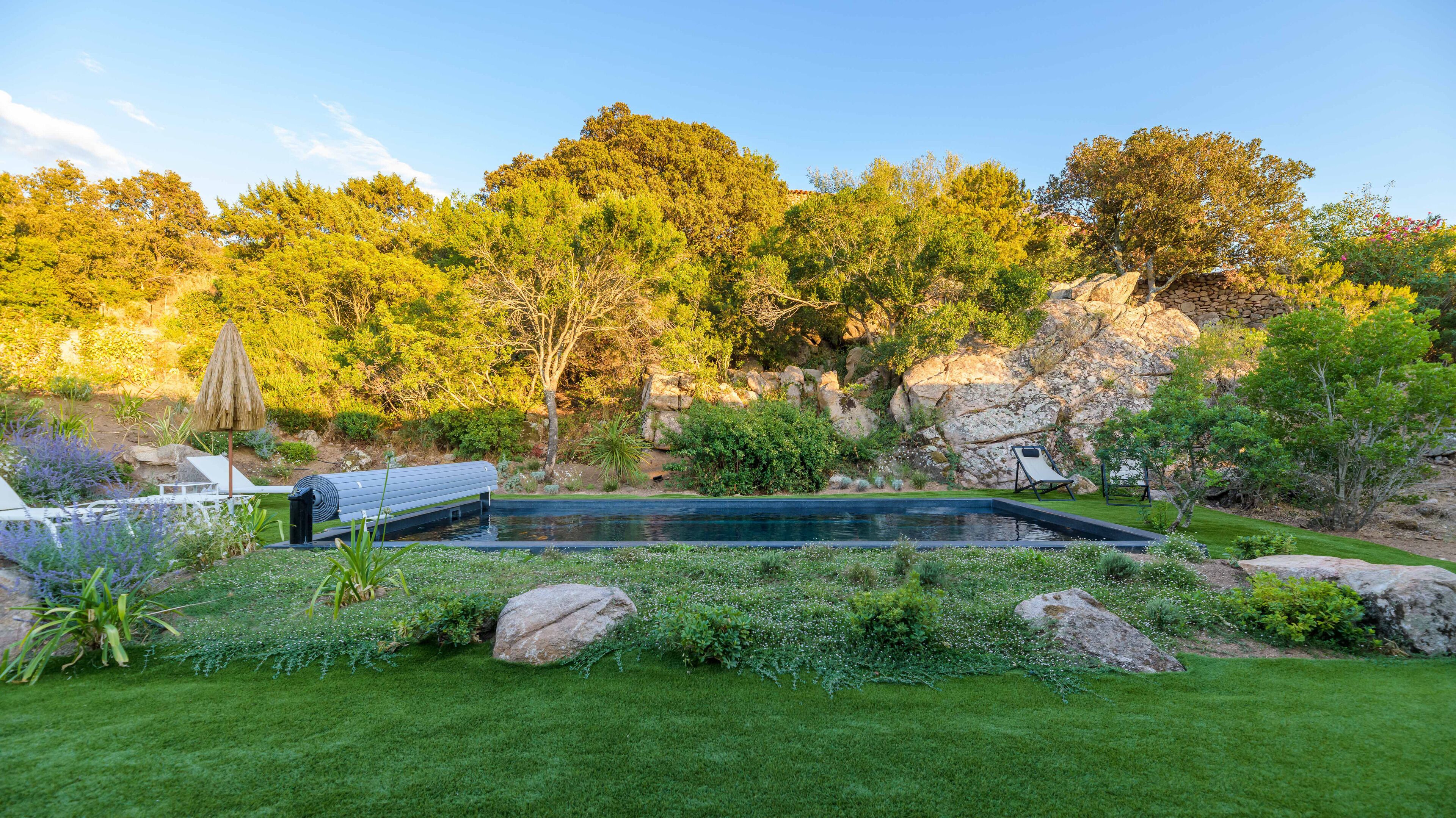 Una piscina con un muro de piedra y follaje al fondo.