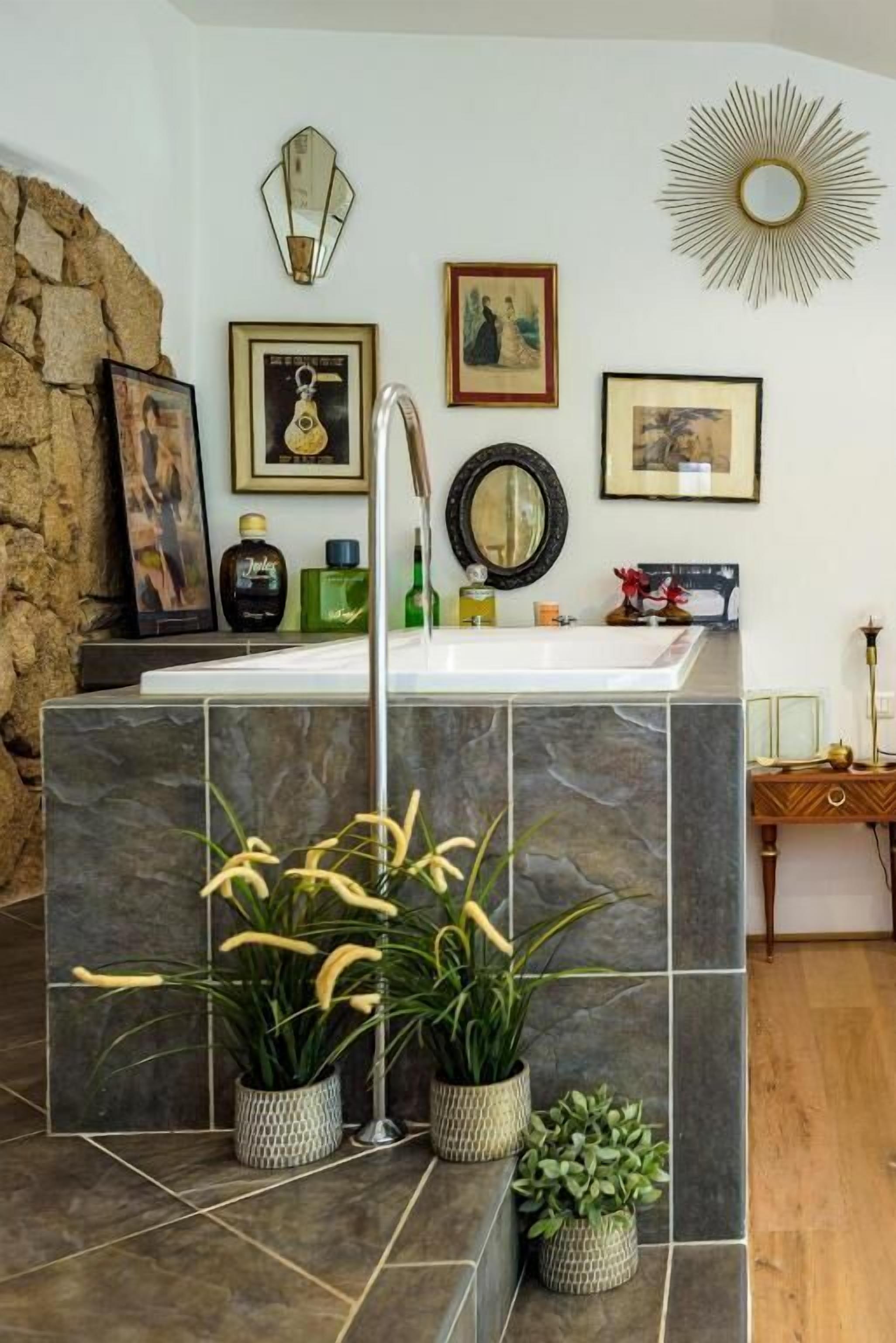 A bathroom with a stone accent wall, a sink with a mirror, and framed artwork on the wall.