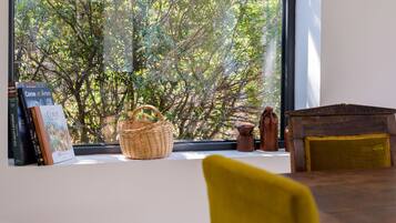 A room with a large window overlooking a tree, a wicker basket, a small wooden chest, and a yellow chair.