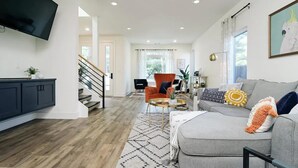 Una sala de estar moderna con un sofá gris, un sillón naranja y un televisor de pantalla plana montado en la pared.