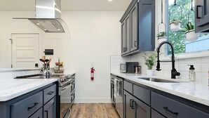 Una cocina moderna con armarios oscuros, una estufa de acero inoxidable, un microondas y un lavamanos con grifo negro.