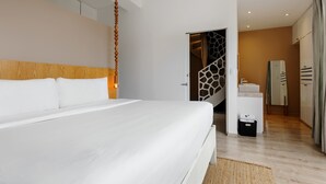 Una moderna camera d'albergo con un letto grande, una testiera in legno, una lampada a sospensione, una scala, un bagno con uno specchio e un portasciugamani, e un pavimento in legno.