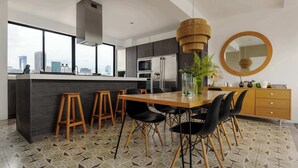 Una cucina moderna con un'isola grande, sgabelli da bar, un tavolo da pranzo con sedie, uno specchio rotondo e vista sulla città attraverso ampie finestre.