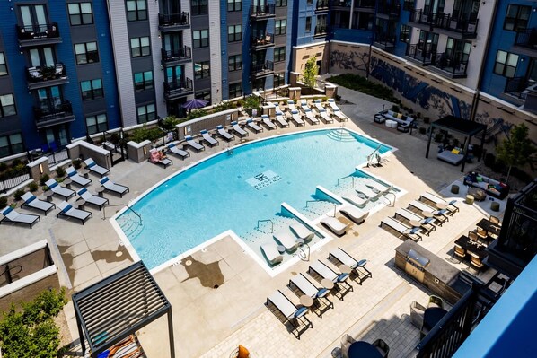 Ein Dachpool mit Liegestühlen und Grillplatz, umgeben von Hochhäusern.