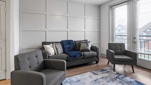 Un salon moderne avec un canapé gris, deux fauteuils et un tapis à motifs.