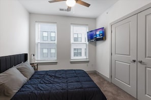 Une chambre à coucher avec un lit, un ventilateur de plafond, un téléviseur fixé au mur et une porte.