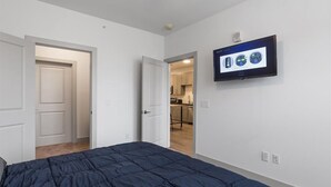 Een slaapkamer met een bed, een aan de muur bevestigde televisie en een deur naar een keuken.