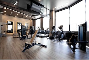 Ein modernes Fitnessstudio mit diversen Trainingsgeräten, großen Fenstern und einer Backsteinwand.