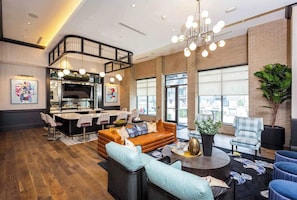 Een moderne hotel lobby met een kitchenette, zithoekjes en grote ramen.