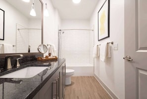 Une salle de bain moderne avec un lavabo en marbre noir, une cabine de douche en verre et des toilettes blanches.