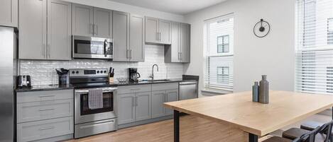 Una cocina moderna con armarios grises, electrodomésticos de acero inoxidable y una mesa de comedor de madera con taburetes de bar.