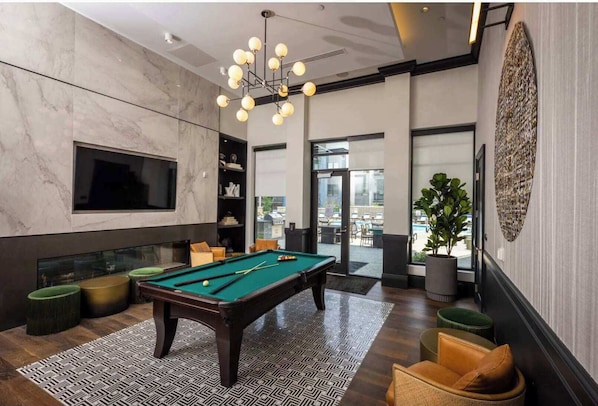 Un espace piscine intérieur moderne, doté d’une table de billard, de sièges confortables et d’une grande fenêtre offrant une vue sur l’extérieur.